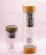Image of two double-walled Teeflaschen by GEVA Vital, featuring wooden lids and built-in stainless steel infusers. The 380ml beige-lidded smaller bottle sits on the left, while the larger 450ml bottle with a wooden lid is on the right. Both bottles display a "GEVA" logo with a tree illustration, highlighting their Premium-Qualität.
