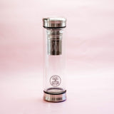 The GEVA Vital Teeflasche Stahl Edition 450ml, a clear glass tea bottle with stainless steel lid and base, infuser, and GEVA logo, offers stylish, plastikfrei 2in1-Teegenuss for unterwegs—shown here against a light pink background.
